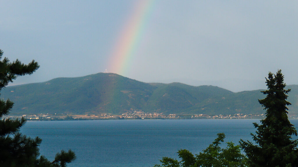 Rainbow over Lake Ohrid in North Macedonia with mountains the background, calm blue water, and trees framing the scenic landscape