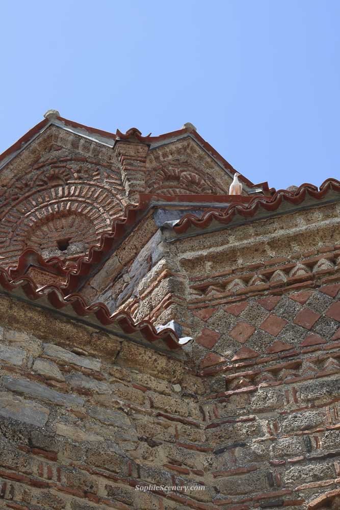 Church of Saint John the Theologian at Kaneo in Ohrid, North-Macedonia, perched on a cliff above Lake Ohrid with crystal-clear blue water and a bright blue sky in de background.