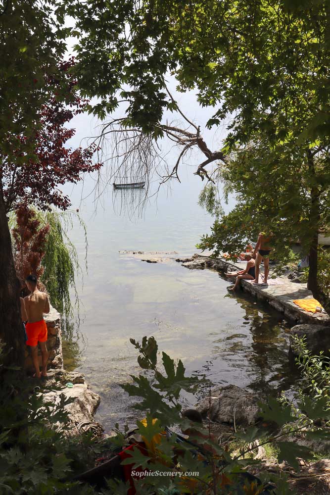 Secret undiscovered beaches near the coastline of Lake Ohrid North-Macedonia. People swimming and jumping into the crystal clear blue water near the coast en-houting the sun between nature and trees