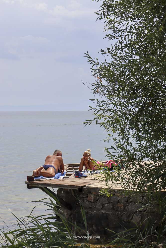 People relaxing and sunbathing on a small wooden platform along the Lake Ohrid coastline Ohrid North-Macedonia, with cal blue lake water greenery and a peaceful summer atmosphere