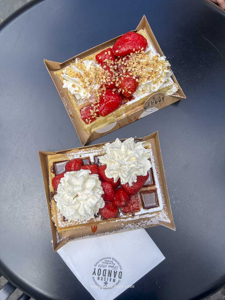 Belgian waffles in Brussels topped with fresh strawberries, whipped cream, chocolate, and powdered sugar on a café table.
