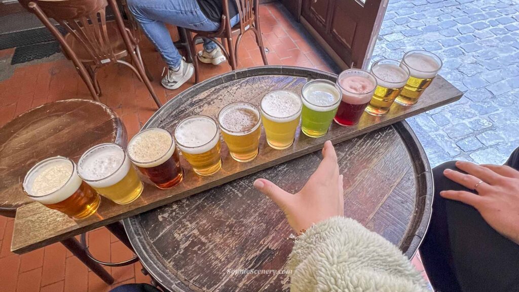 Girl reaching for a Belgian beer from a traditional beer meter in a Brussels pub, with multiple local beers lined up on a wooden tasting board.