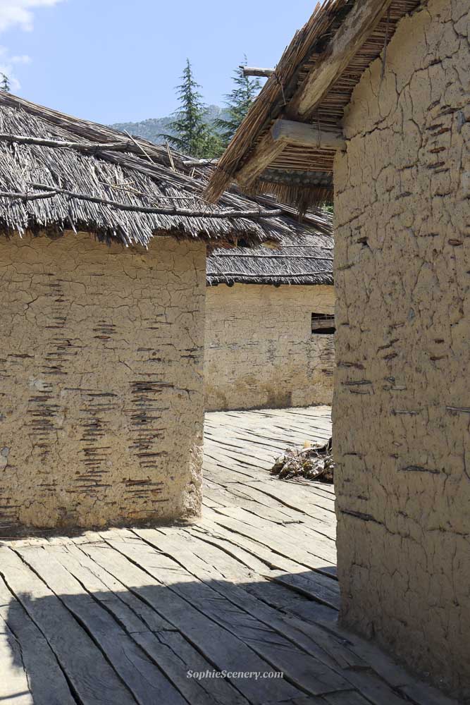 Bay of Bones open-air Museum on Lake Ohrid in North-Macedonia, showing reconstructed wooden houses built over turquoise water with mountains and greenery in the background on a sunny day