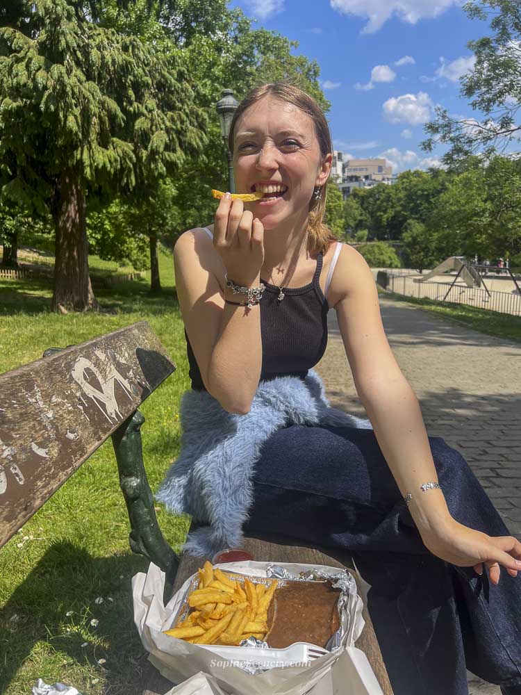 Girl eating traditional Belgian fries in Brussels, holding a cone of crispy golden fries with sauce while exploring the city.