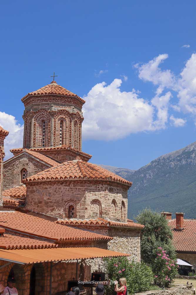 St. Naum Monastery in Ohrid, North Macedonia, featuring a historic stone church with orange tiled roofs, mountains the background green gardens and a bright blue sky on a sunny day