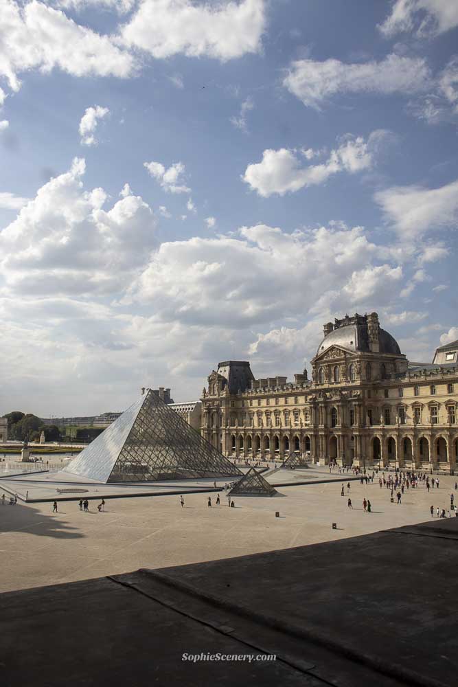 Exterior of the Louvre Museum glass pyramid and historic palace in Paris under a blue sky, symbolizing free entry for EU residents under 26 years old.