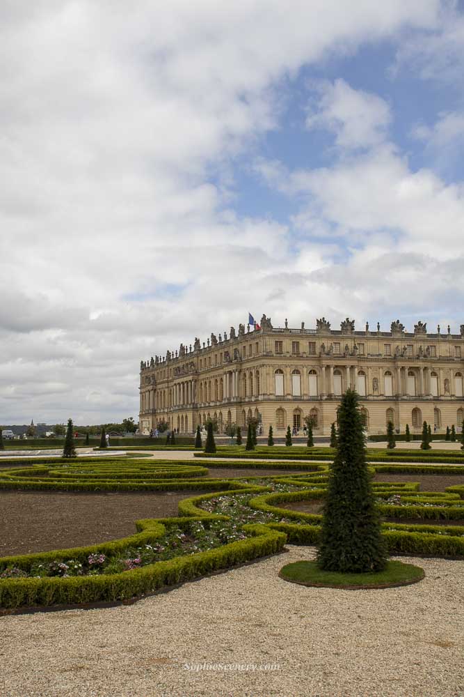 Gardens of the Palace of Versailles with manicured lawns and fountains, and the château visible in the background under a blue sky, highlighting free entry for under-26 EU citizens.