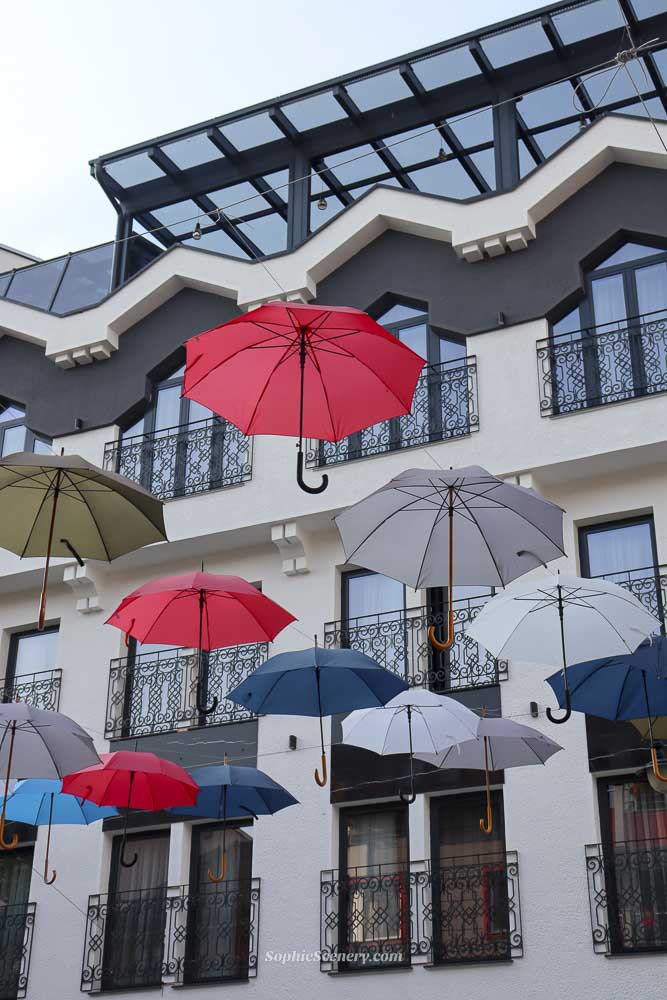Colorful umbrellas hanging above a street in Struga, creating a vibrant walkway leading toward a local market in North Macedonia.